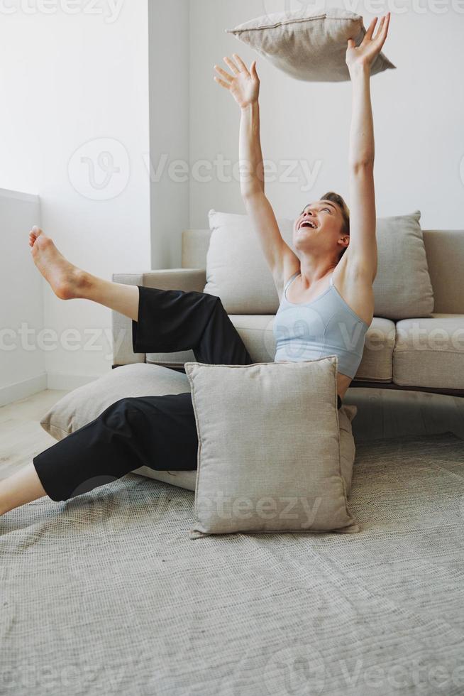 Teenager Mädchen Lächeln jedermann sitzt beim Zuhause in der Nähe von das Couch und wirft oben Kissen, Spaß Spiel und Glück ohne Filter, Kopieren Platz foto