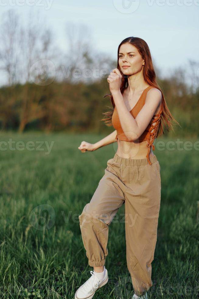 ein Frau von sportlich bauen läuft durch das Park auf das Grün Gras mit lose, fliegend Haar und Arbeiten aus in das Sonnenuntergang Licht foto