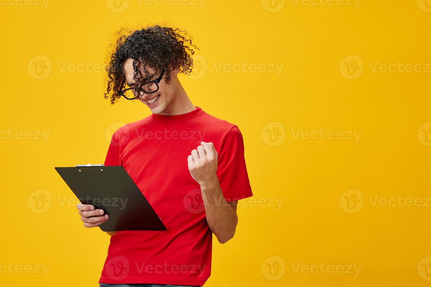 froh glücklich kurzsichtig jung Schüler Mann im rot T-Shirt komisch Brillen hält Tablette Mappe mit Studie Anmerkungen posieren isoliert auf Über Gelb Studio Hintergrund. kostenlos Platz zum Anzeige. Bildung Hochschule Konzept foto