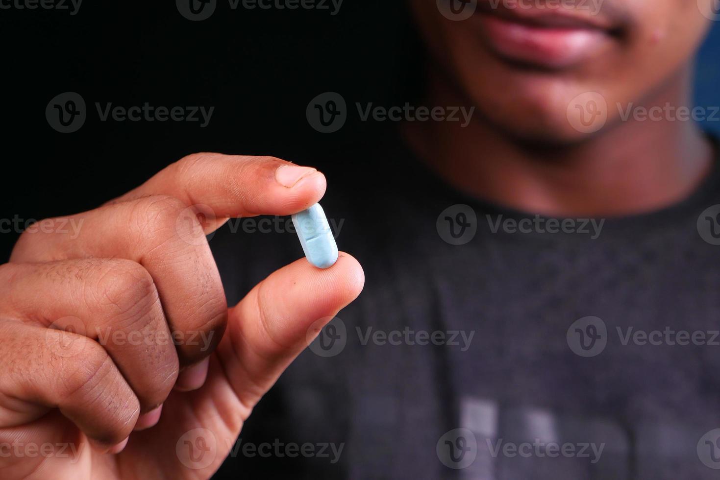 Nahaufnahme eines jungen Mannes, der eine blaue Pille hält foto