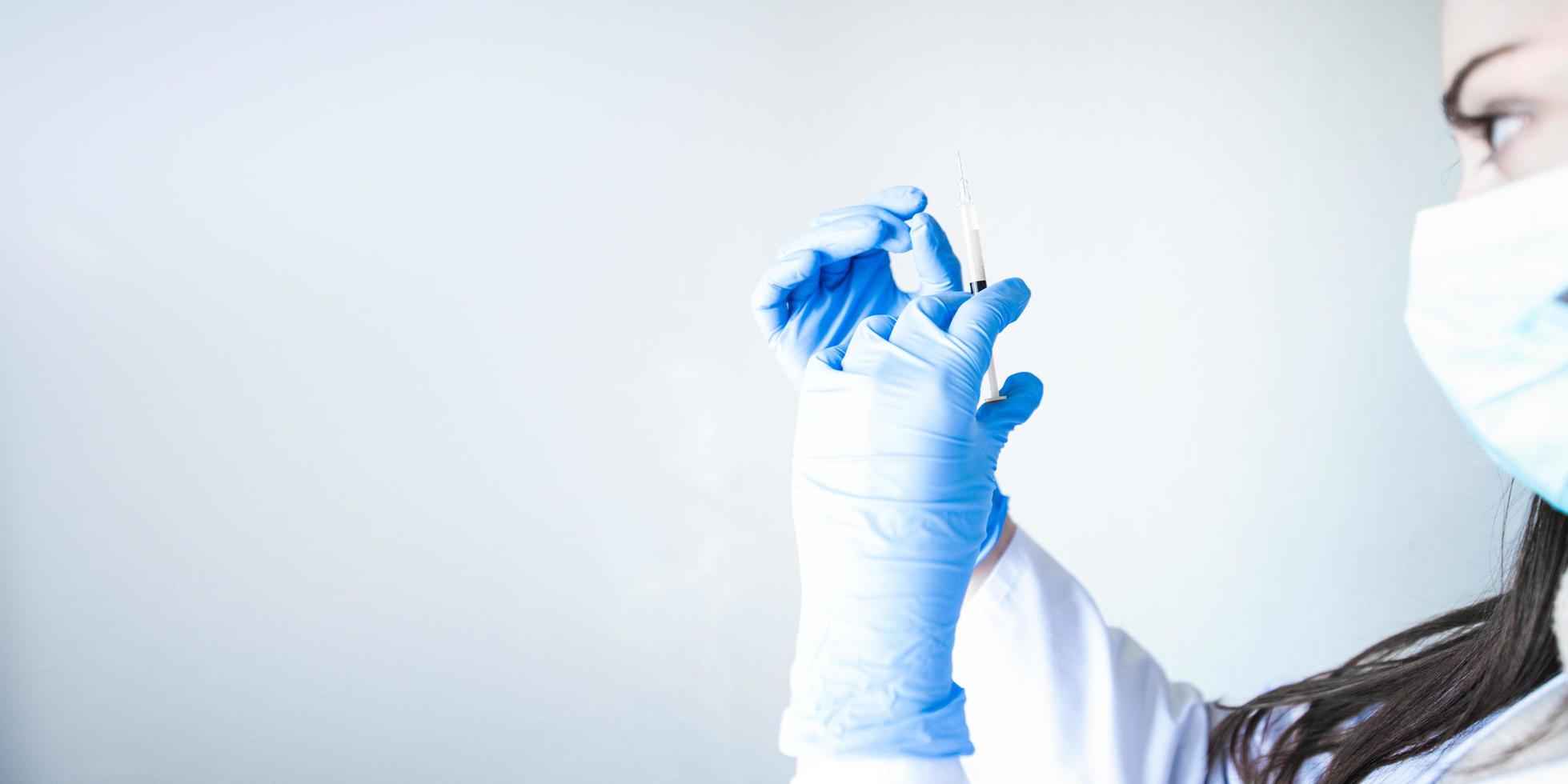 Krankenschwester im Profil, das Impfstoff mit blauen Handschuhen auf weißem Hintergrund mit Platz für Text hält foto