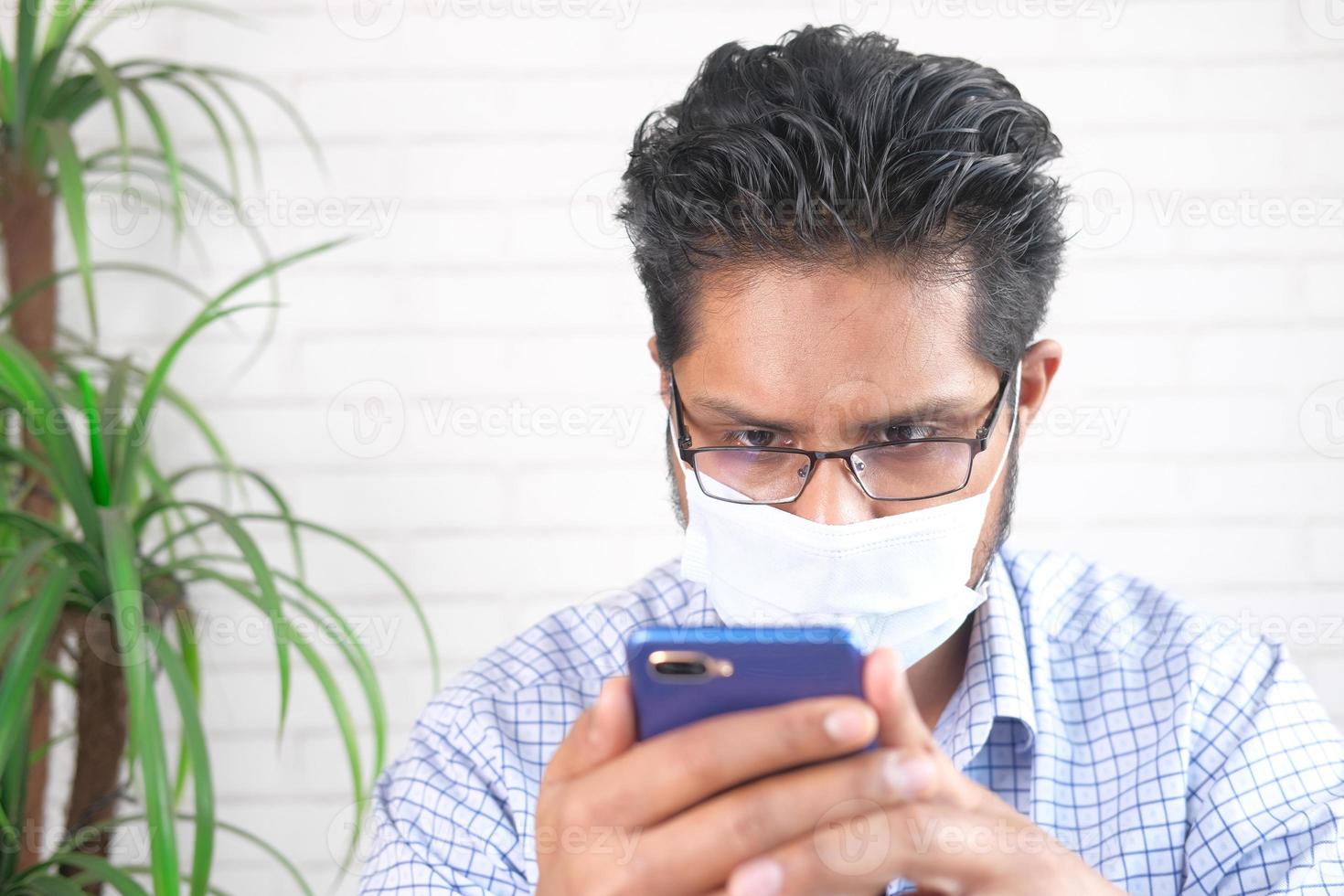 Mann, der eine Maske trägt und Telefon ansieht foto