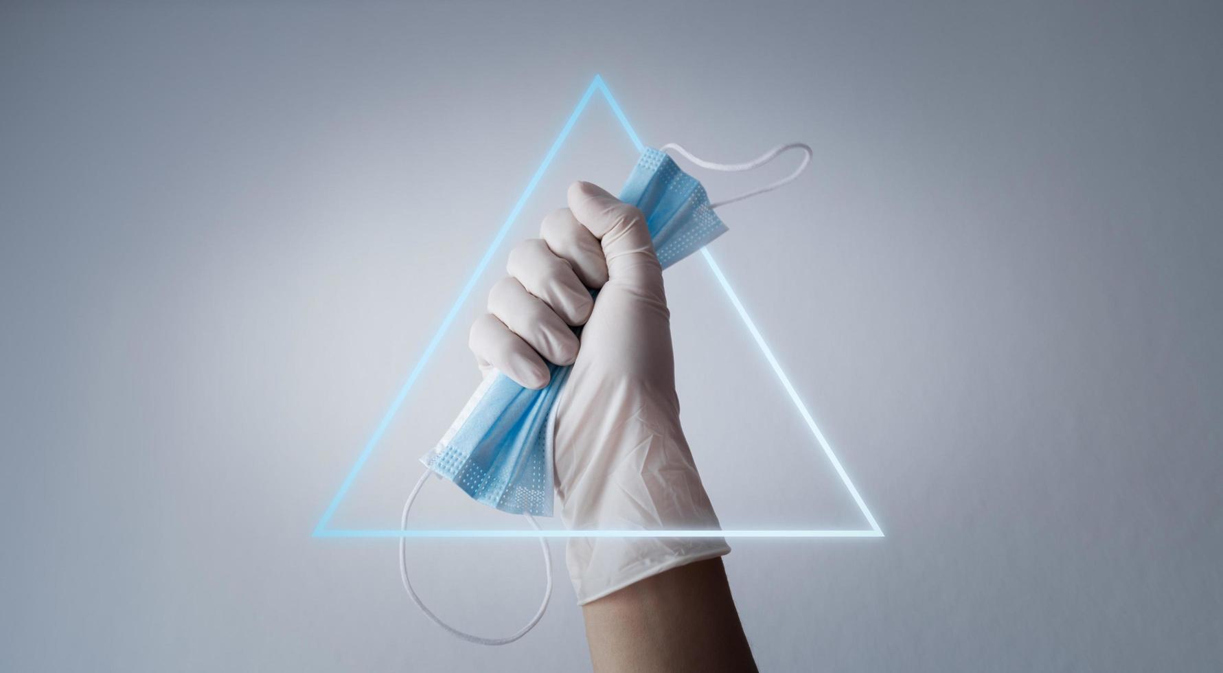 Hand hält Schutzmaske mit Handschuh und hellem Dreieck foto