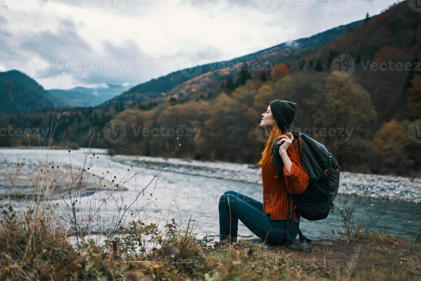 Frau in der Nähe von das Fluss im das Berge mit ein Rucksack auf ihr Schultern sind ruhen im das Herbst Wald foto