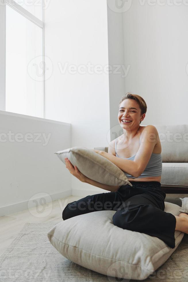 Teenager Mädchen Lächeln jedermann sitzt beim Zuhause in der Nähe von das Couch und wirft oben Kissen, Spaß Spiel und Glück ohne Filter, Kopieren Platz foto