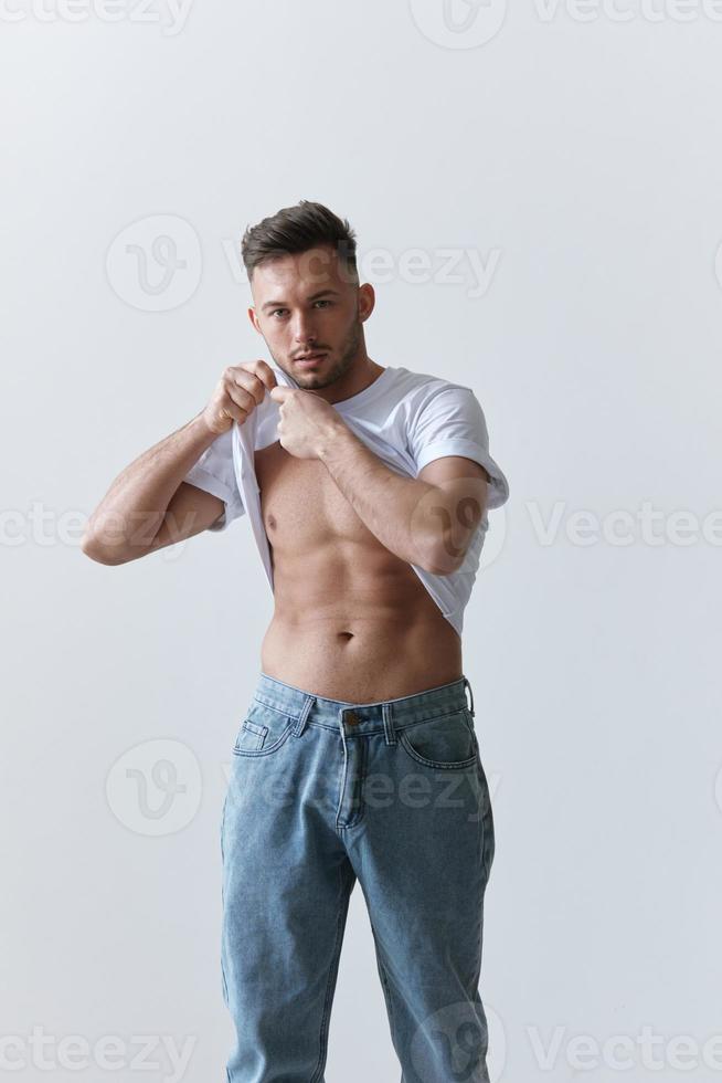 Porträt Schuss von gut aussehend sexy flirten Braun gebrannt Mann Kerl erziehen Basic T-Shirt sieht aus beim Kamera posieren auf Weiß Hintergrund. Mode Stil Neu Sammlung Angebot. Kopieren Raum zum Anzeige. Modell- einrasten foto