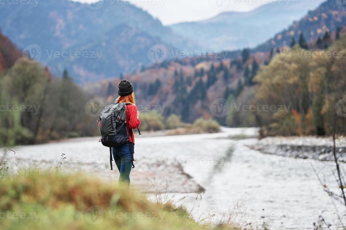 Frau im ein rot Sweatshirt mit ein Rucksack im das Berge auf Natur in der Nähe von das Fluss Teich See foto