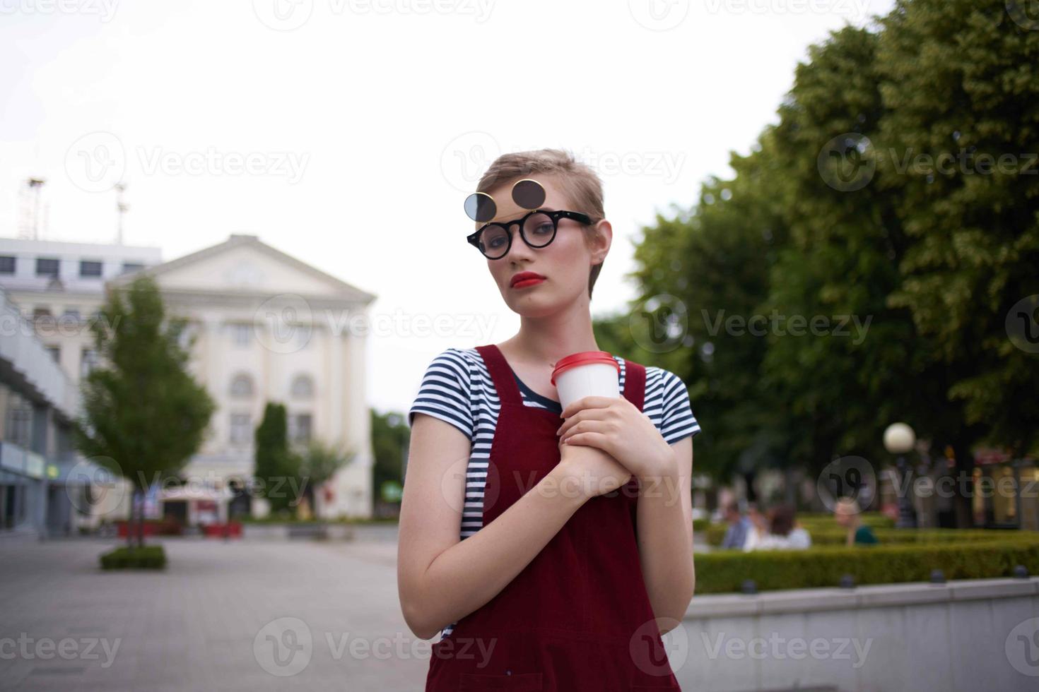 ein Frau mit Brille Spaziergänge um das Stadt ein Glas mit ein trinken Freizeit Kommunikation foto