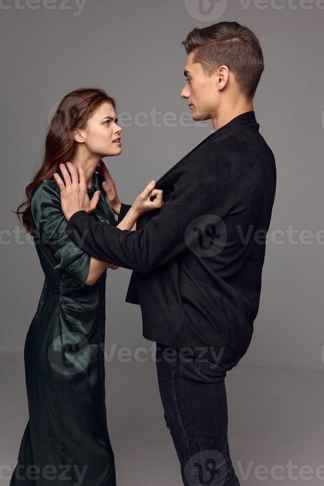 Frau halten ein Mann hinter ein Jacke auf ein grau Hintergrund empört aussehen Stress Konflikt foto