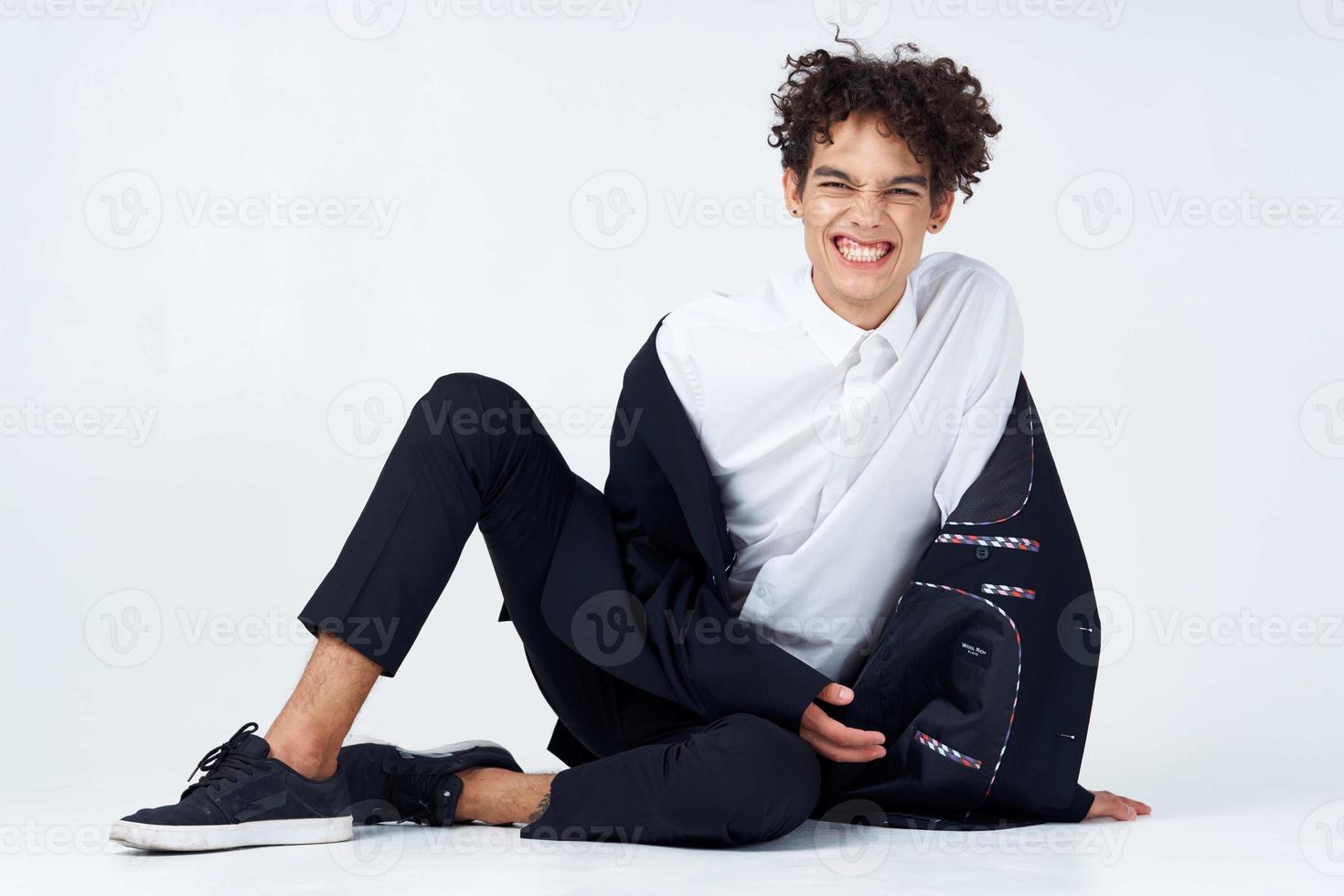 Kerl im ein Weiß Hemd Sitzung auf das Fußboden lockig Haar foto