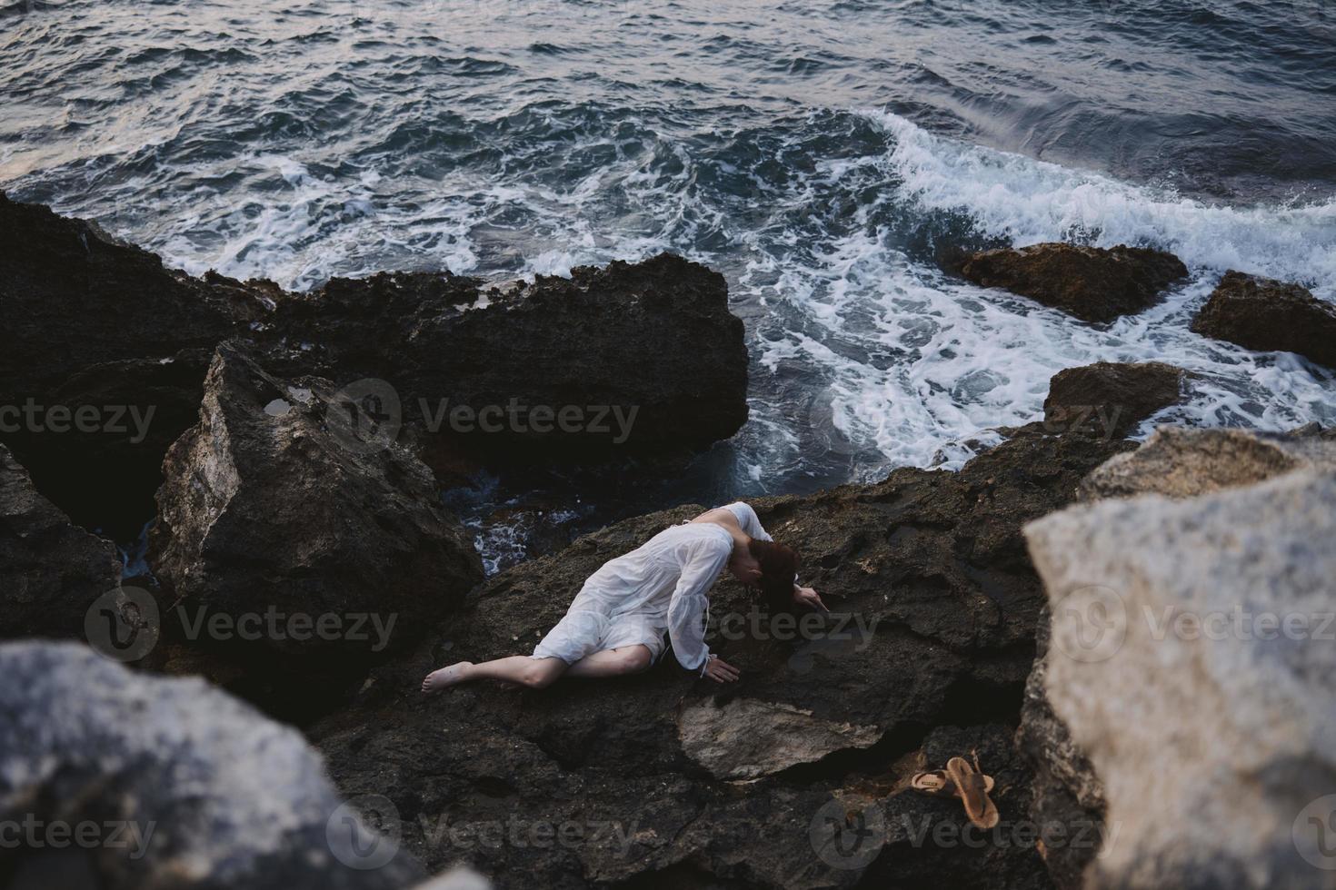 schön jung Frau im ein Weiß Kleid Lügen auf ein Stein im ein Weiß Kleid Landschaft foto