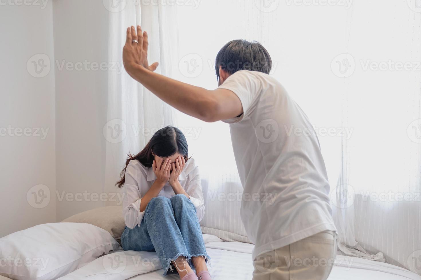 intern Gewalt. Familie Konflikt Männer Attacke und schlagen Frauen beim heim. erschrocken Frau Abdeckung ihr Gesicht Sitzung auf das Bett. sie war verängstigt. foto