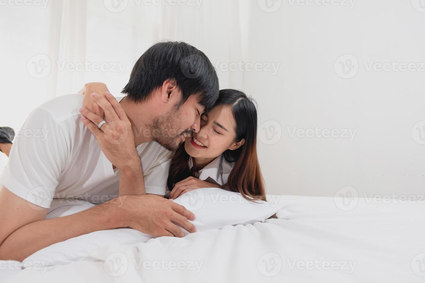 glücklich jung asiatisch Paar umarmen, neckisch, spielen fröhlich im Bett beim heim, romantisch Zeit zu verbessern Familie Verbindung. Familie Konzept. foto