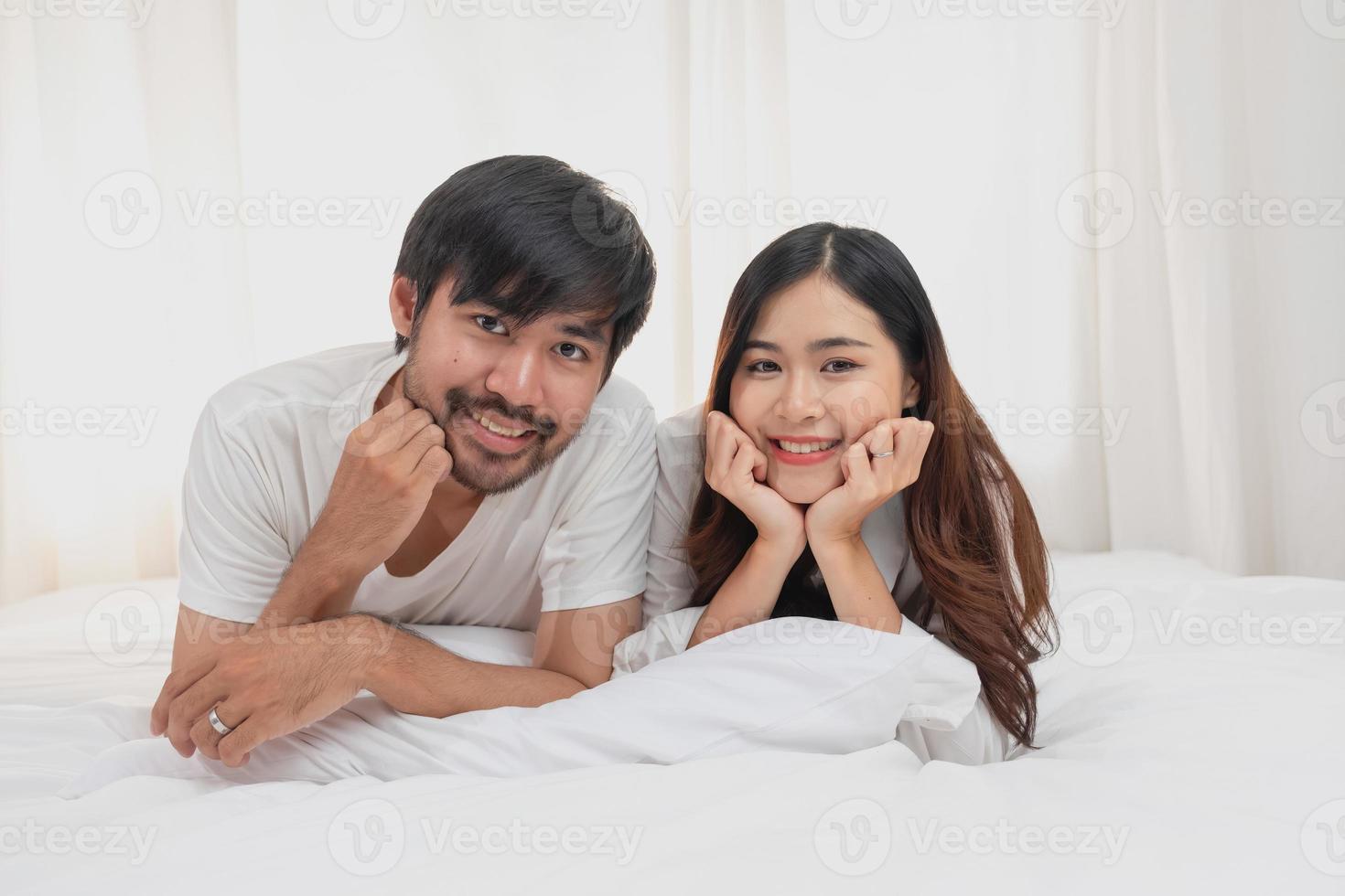 glücklich jung asiatisch Paar umarmen, neckisch, spielen fröhlich im Bett beim heim, romantisch Zeit zu verbessern Familie Verbindung. Familie Konzept. foto