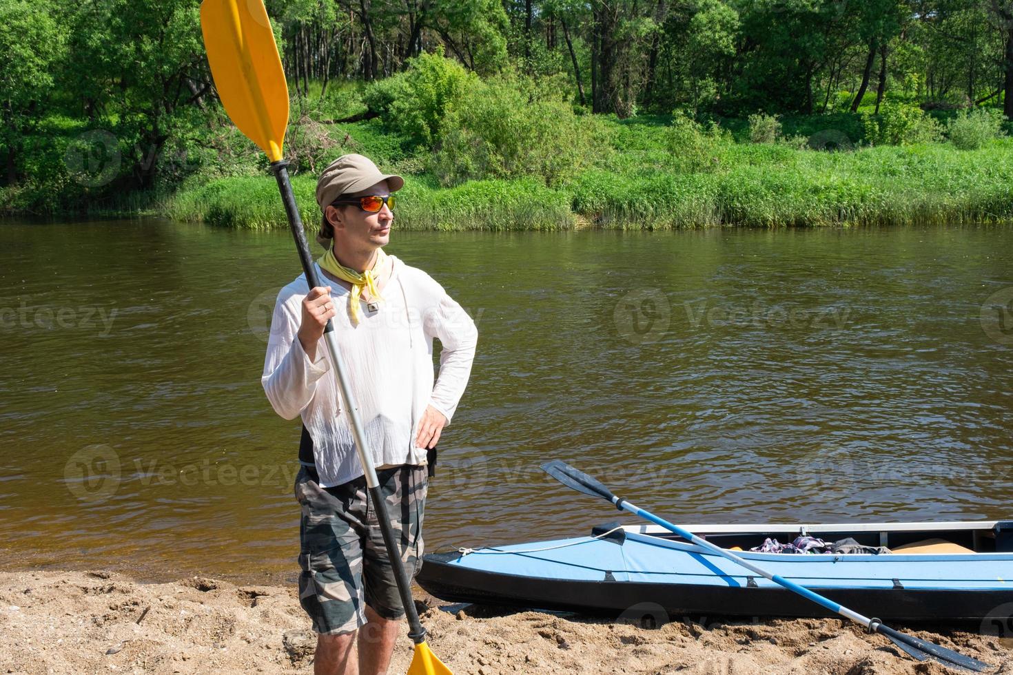 ein Mann mit ein Kajak Paddel zum Rafting steht auf das Fluss Bank. Sport Wasser Wanderung, ein Sommer- Abenteuer. umweltfreundlich und extrem Tourismus, aktiv und gesund Lebensstil foto