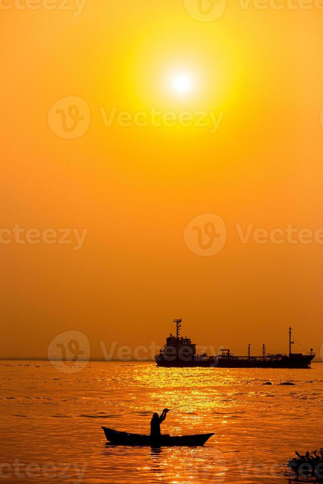 Abend golden Sonnenuntergang Zeit, ein Fischer Angeln auf das Strand auf ein Boot. foto