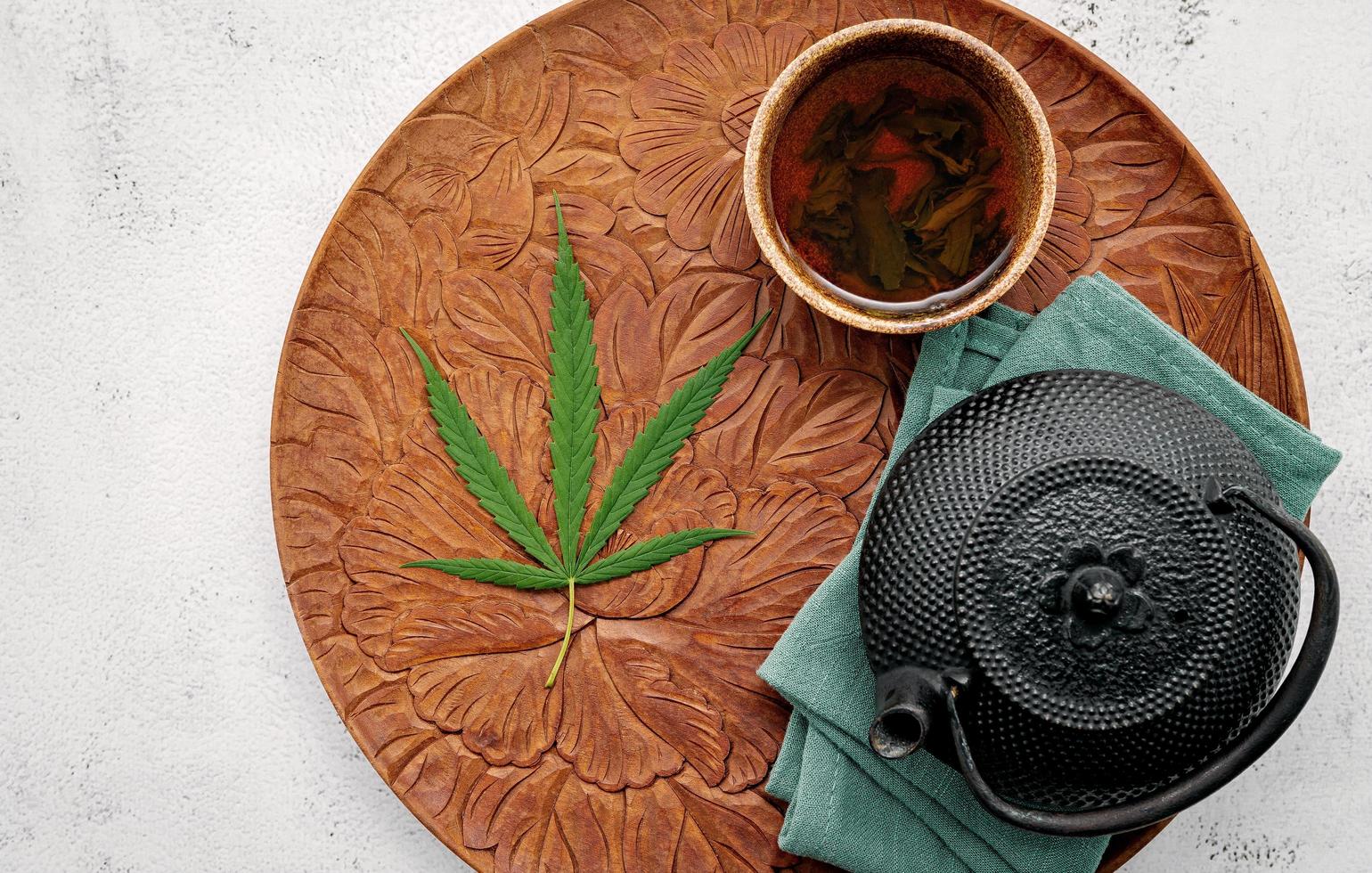 Weinlese-Teekanne mit Cannabis-Kräutertee und frischen Marihuana-Blättern, die auf Betonhintergrund aufgestellt werden foto