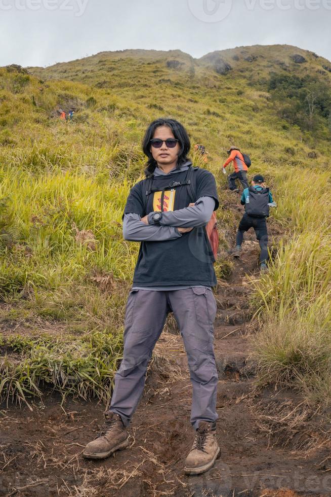 Mann Wandern zu das oben Berg, mit Savana Spur und wolkig Schwingungen. das Foto ist geeignet zu verwenden zum Abenteuer Inhalt Medien, Natur Poster und Wald Hintergrund.