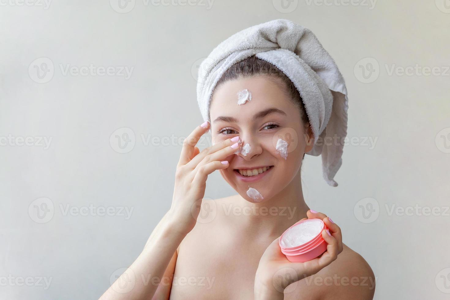 Schönheitsporträt einer Frau im Handtuch auf dem Kopf mit weißer pflegender Maske oder Creme im Gesicht, weißer Hintergrund isoliert foto