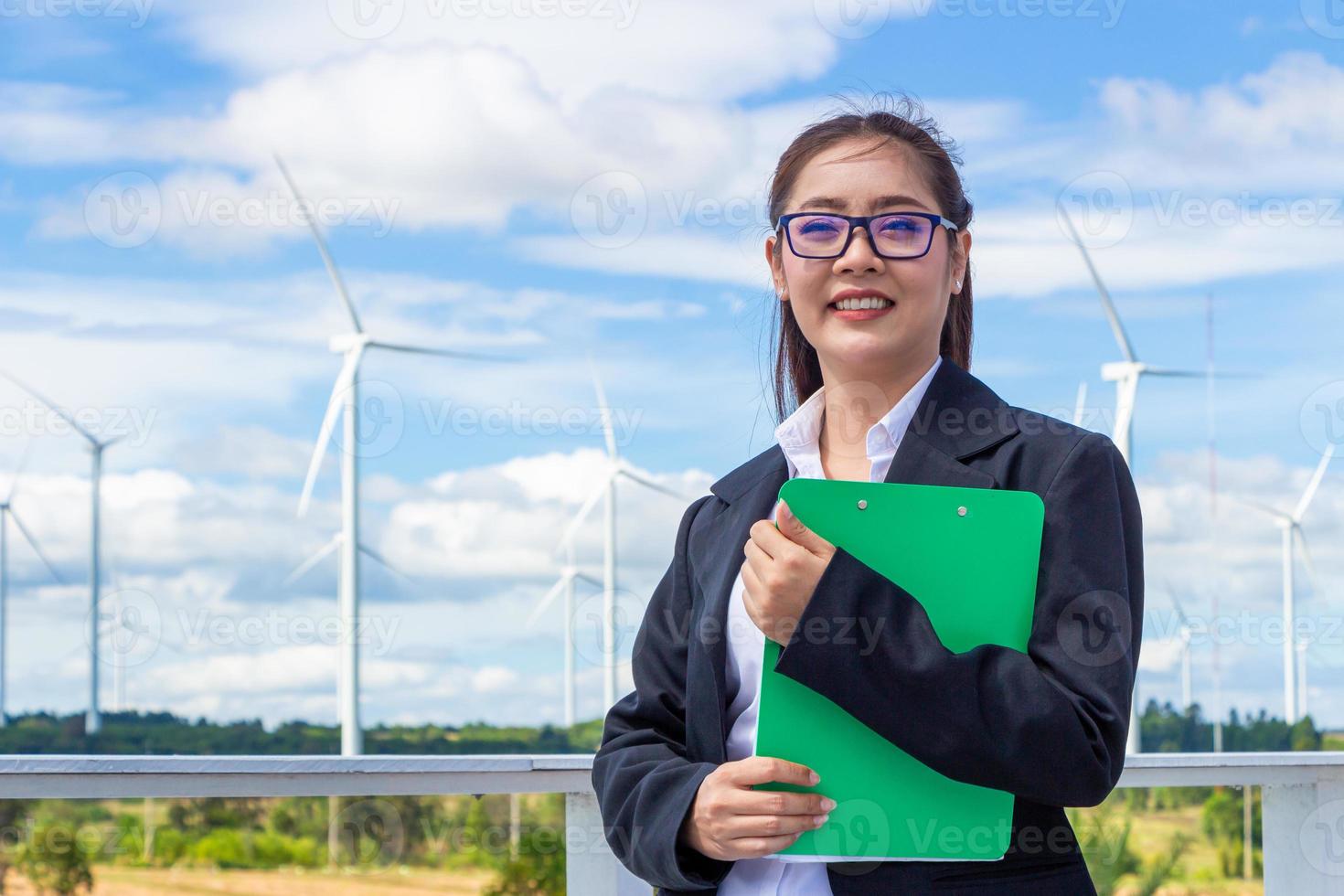 Energie Ingenieur weiblich Arbeiten beim Wind Bauernhof. asiatisch Geschäft Frau tragen passen halten Tablette und Zwischenablage mit Windmühle Umgebung verlängerbar Energie. foto