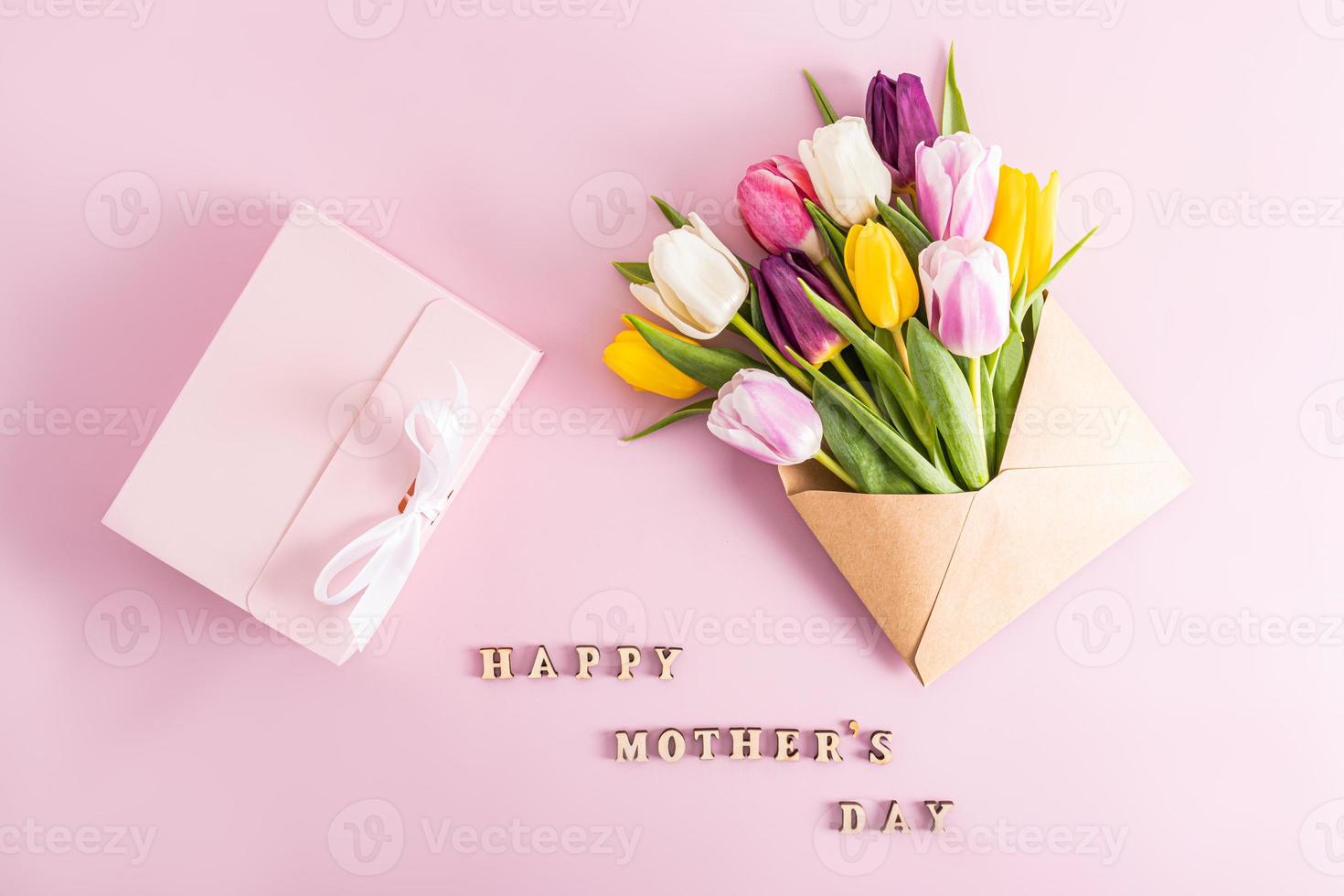 ein festlich Komposition zum Mutter Tag. schön bunt Frühling Tulpen im ein Kunst Briefumschlag und ein Rosa Box mit ein Geschenk. oben Sicht. Text. foto