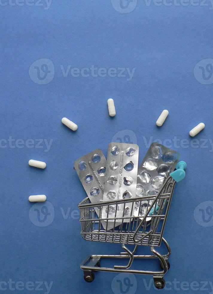 Einkaufen Wagen mit leeren Tabletten Verpackung und Medizin Tabletten auf Blau Hintergrund. COVID-19. das Konzept von hoffen und das Ende von Quarantäne. kreativ Idee zum online Apotheke und pharmazeutische Unternehmen. foto