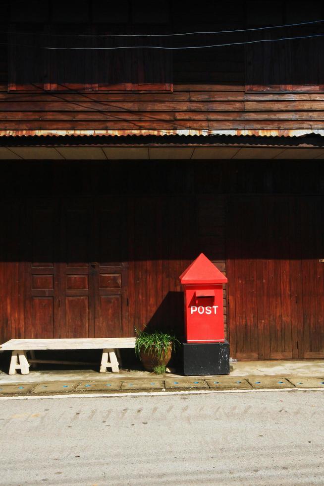 rot Briefkasten auf Fußweg in der Nähe von alt hölzern Haus beim Landschaft im Thailand foto