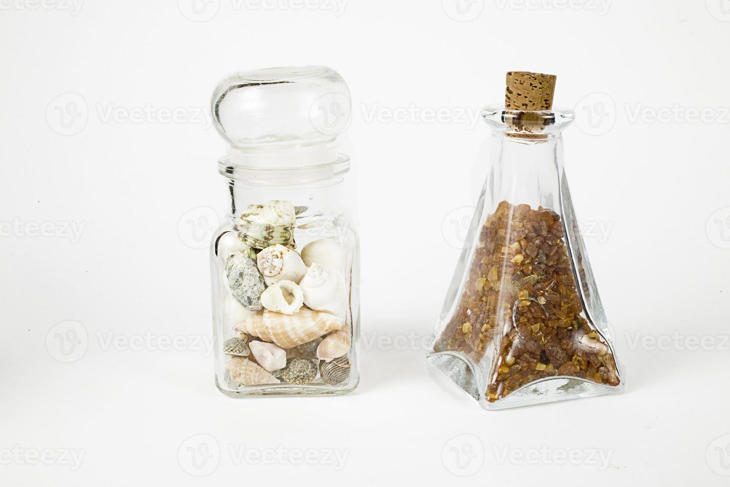 Glas Behälter gefüllt mit natürlich fein Bernsteine und Muscheln auf ein Weiß Hintergrund foto