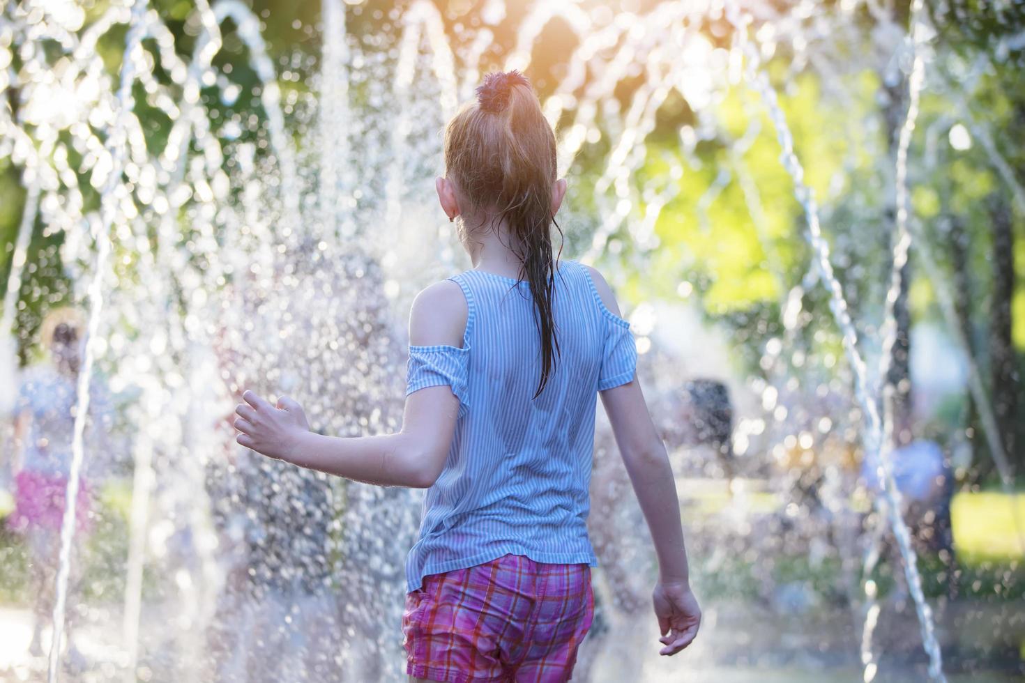 nass Mädchen sieht aus beim das Brunnen. Kind auf ein heiß Tag beim das Stadt Brunnen. foto