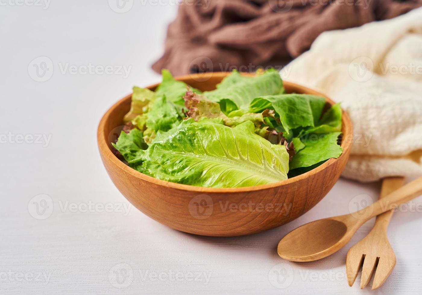 frisch Salat von Grün Blätter im ein hölzern Schüssel auf Weiß sauber Stimmung Hintergrund mit Kopieren Raum. Löffel und Gabel foto