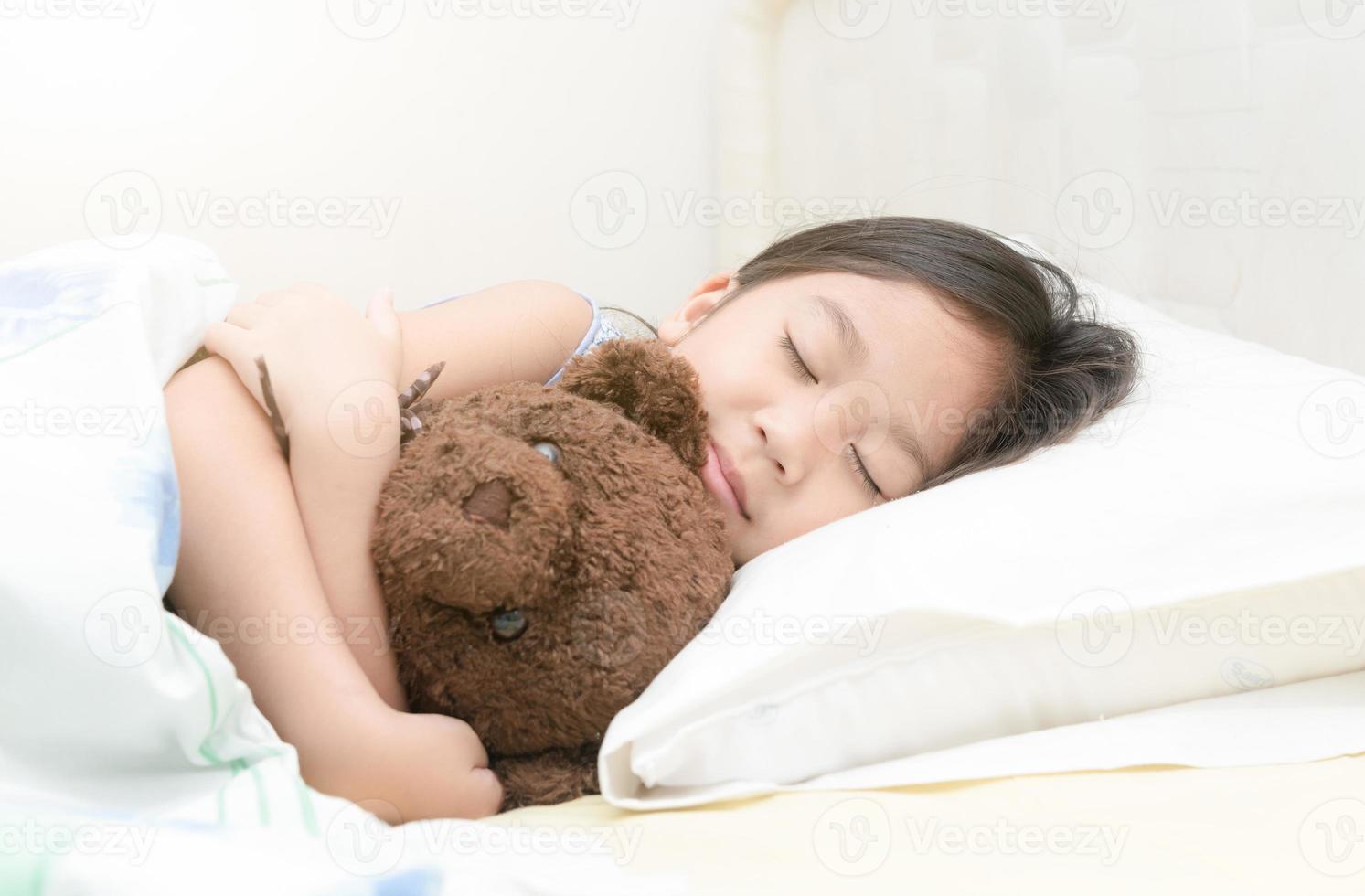 süß wenig asiatisch Mädchen Schlaf und Umarmung Teddy Bär auf Bett foto