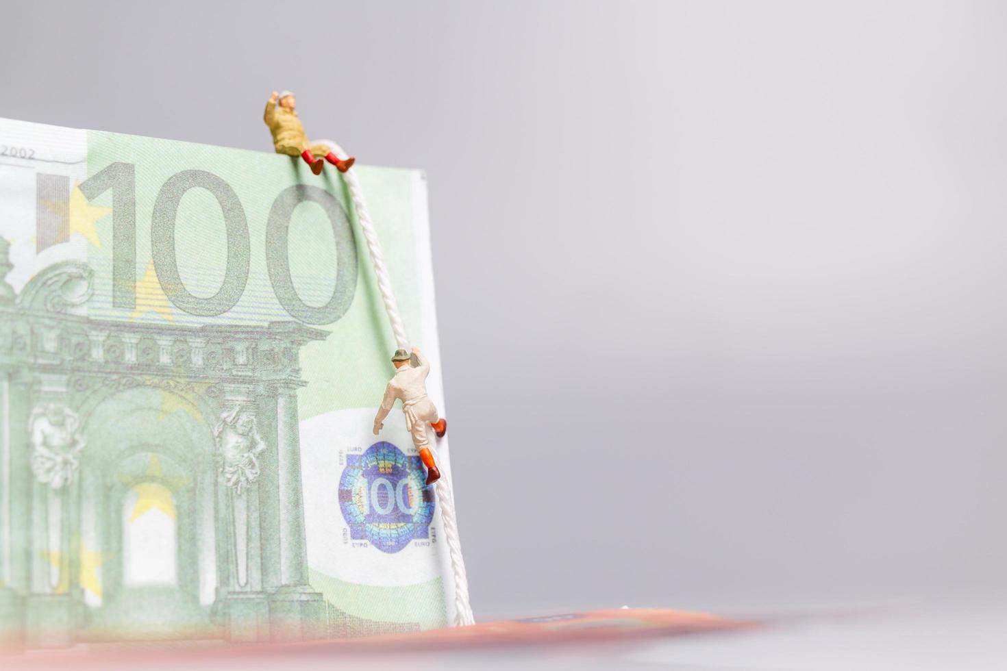 Miniaturmenschen, Kletterer klettert auf eine Euro-Banknote, Geschäftskonzept. foto