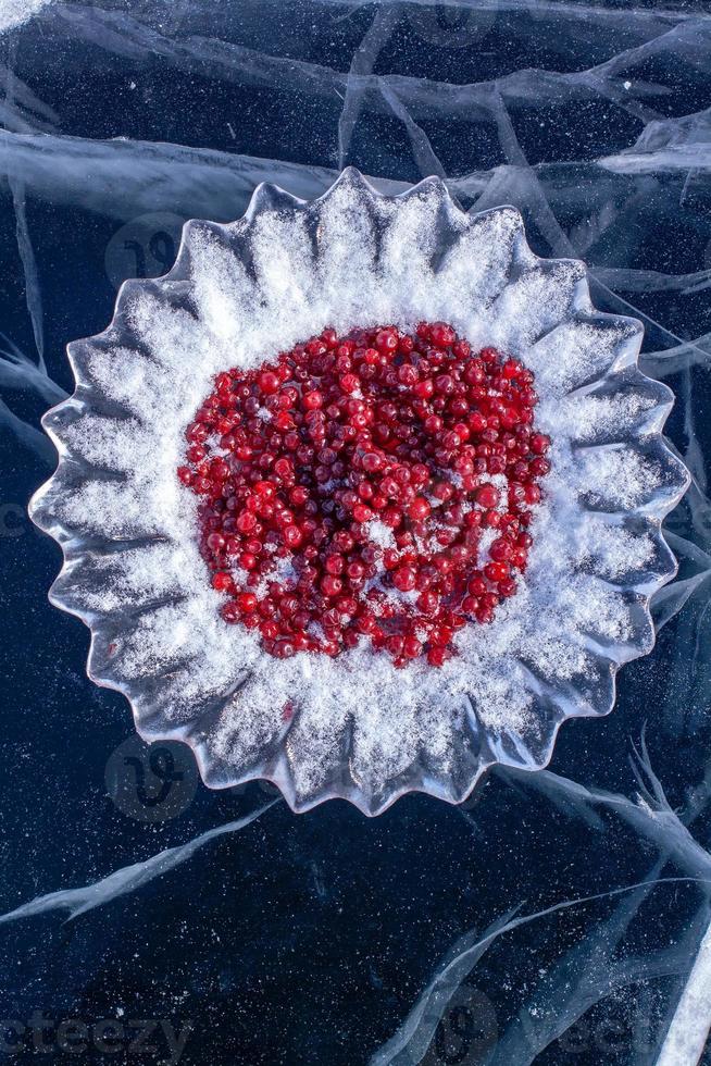 ein Eis Gericht mit Preiselbeeren bestreut mit Schnee auf das Eis von See Baikalsee. Eis mit tief Risse. rot Beeren auf Eisschnitt Teller. Russisch sibirisch Benutzerdefiniert von Treffen Gäste auf See Baikalsee. Vertikale. foto