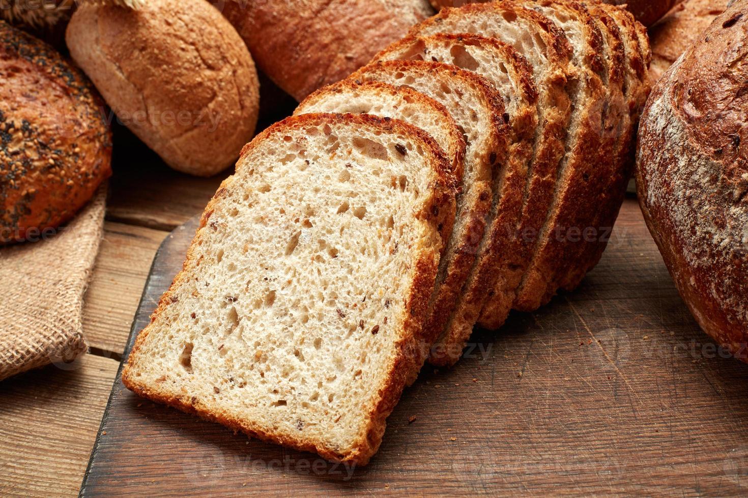 Haufen von ganzem und geschnittenem frisch gebackenem Brot auf hölzernem Hintergrund foto