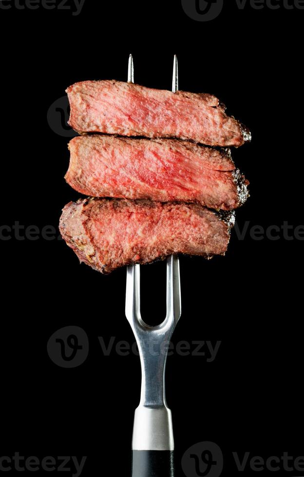 frisches gegrilltes Steak auf Gabel auf schwarzem Hintergrund foto