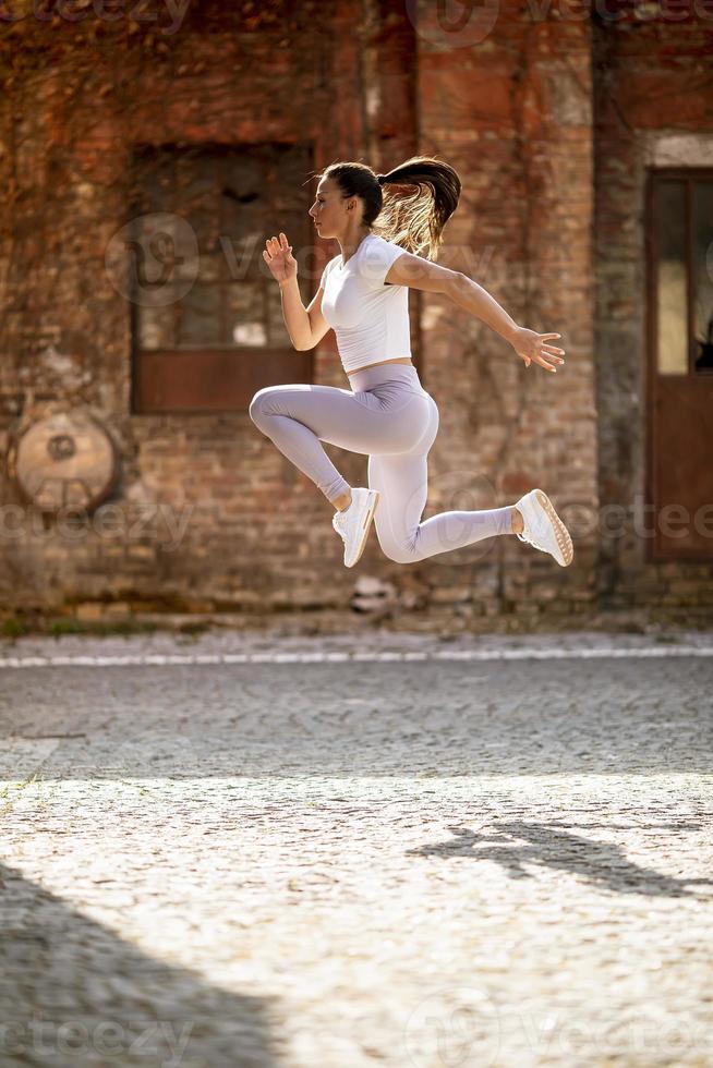 hübsche junge Frau, die während des Trainings in der städtischen Umgebung hoch springt foto