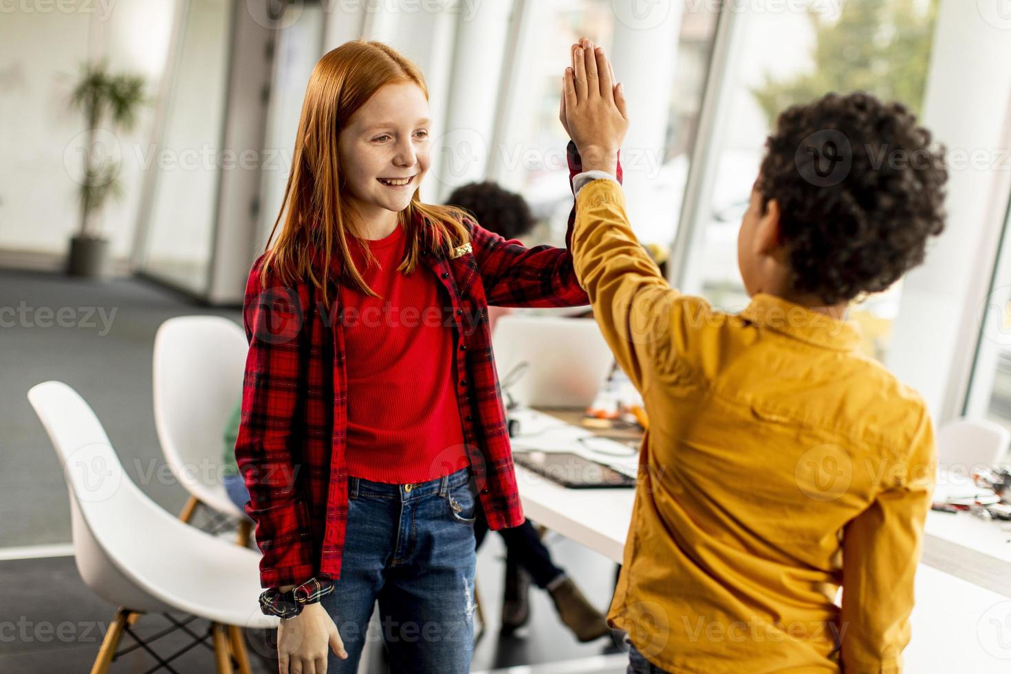 süße kleine Freunde, die vor einer Gruppe von Kindern stehen, die elektrisches Spielzeug und Roboter im Robotikklassenzimmer programmieren foto