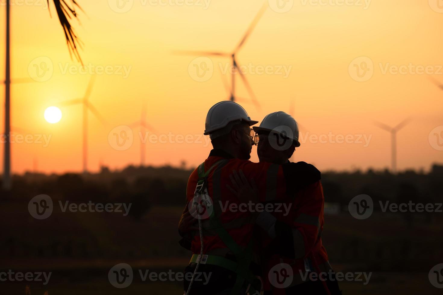 Ingenieure Arbeiten auf Wind Bauernhöfe zum verlängerbar Energie sind verantwortlich zum Aufrechterhaltung groß Wind Turbinen. Rückkehr von Arbeit während während das Abend Sonne scheint ein schön golden Licht auf beide von foto