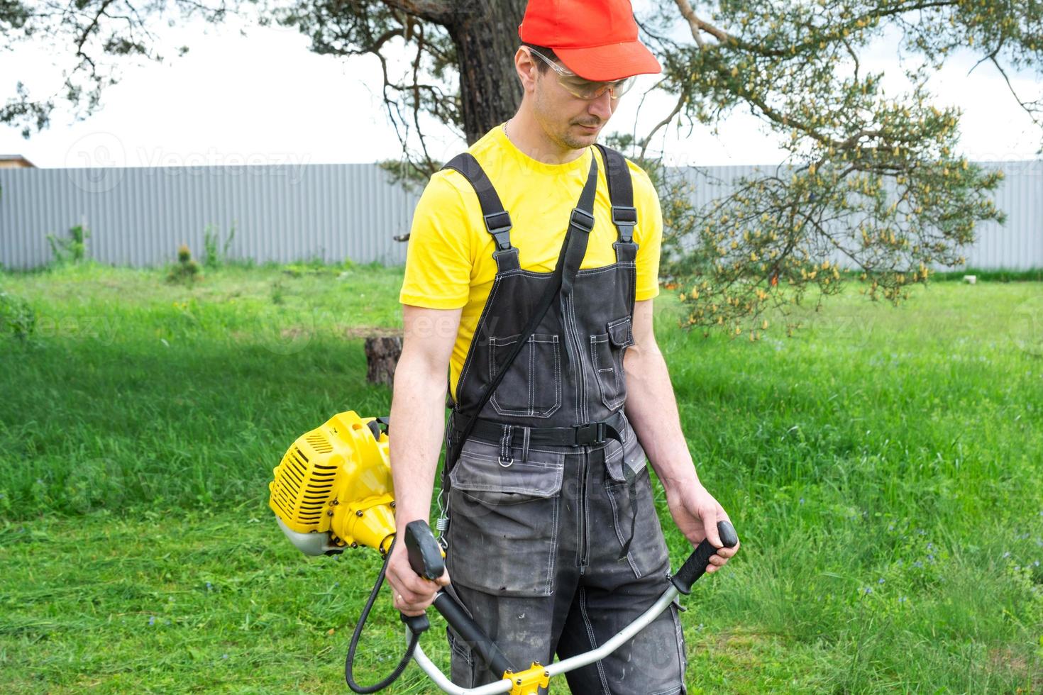 ein männlich Gärtner mäht das Grün Gras von das Rasen im das Hinterhof mit ein Benzin Mäher. Trimmer zum das Pflege von ein Garten Handlung foto