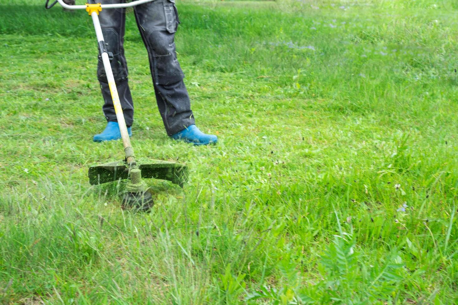 ein männlich Gärtner mäht das Grün Gras von das Rasen im das Hinterhof mit ein Benzin Mäher. Trimmer zum das Pflege von ein Garten Handlung foto