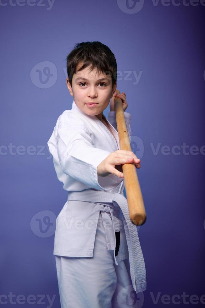 zuversichtlich stark konzentriert Junge - - Aikido Ringer - - im ein Kimono steht mit ein hölzern jo Waffe im seine Hände. orientalisch kriegerisch Kunst trainieren Konzept foto