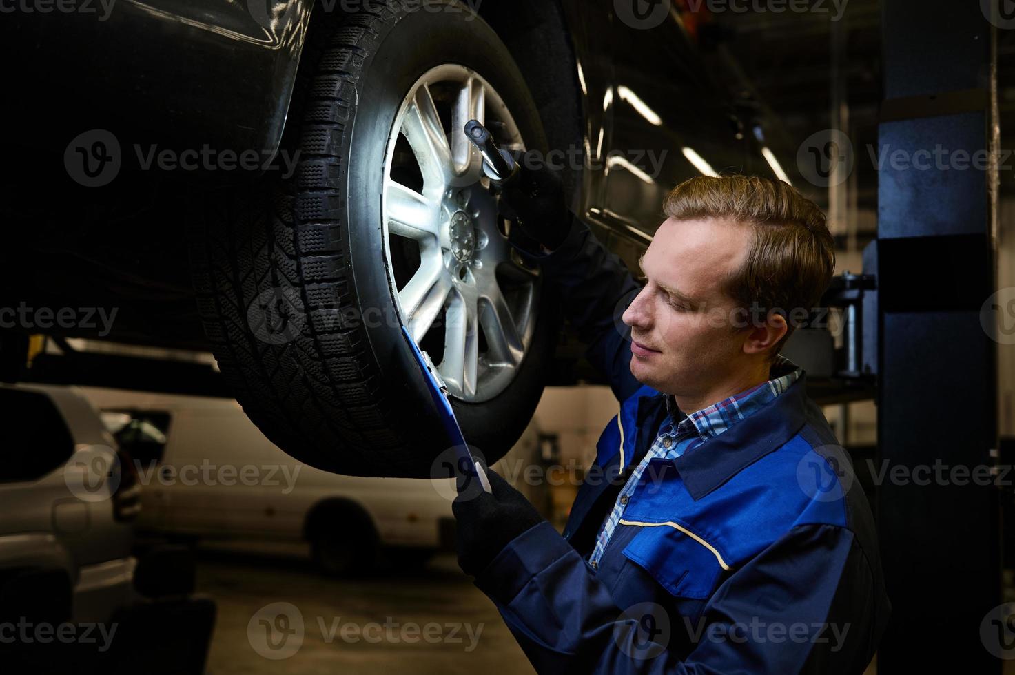 Auto Mechaniker im Auto Reparatur Geschäft Herstellung Checkliste zum reparieren ein angehoben modern Auto während Garantie Bedienung und technisch Inspektion foto