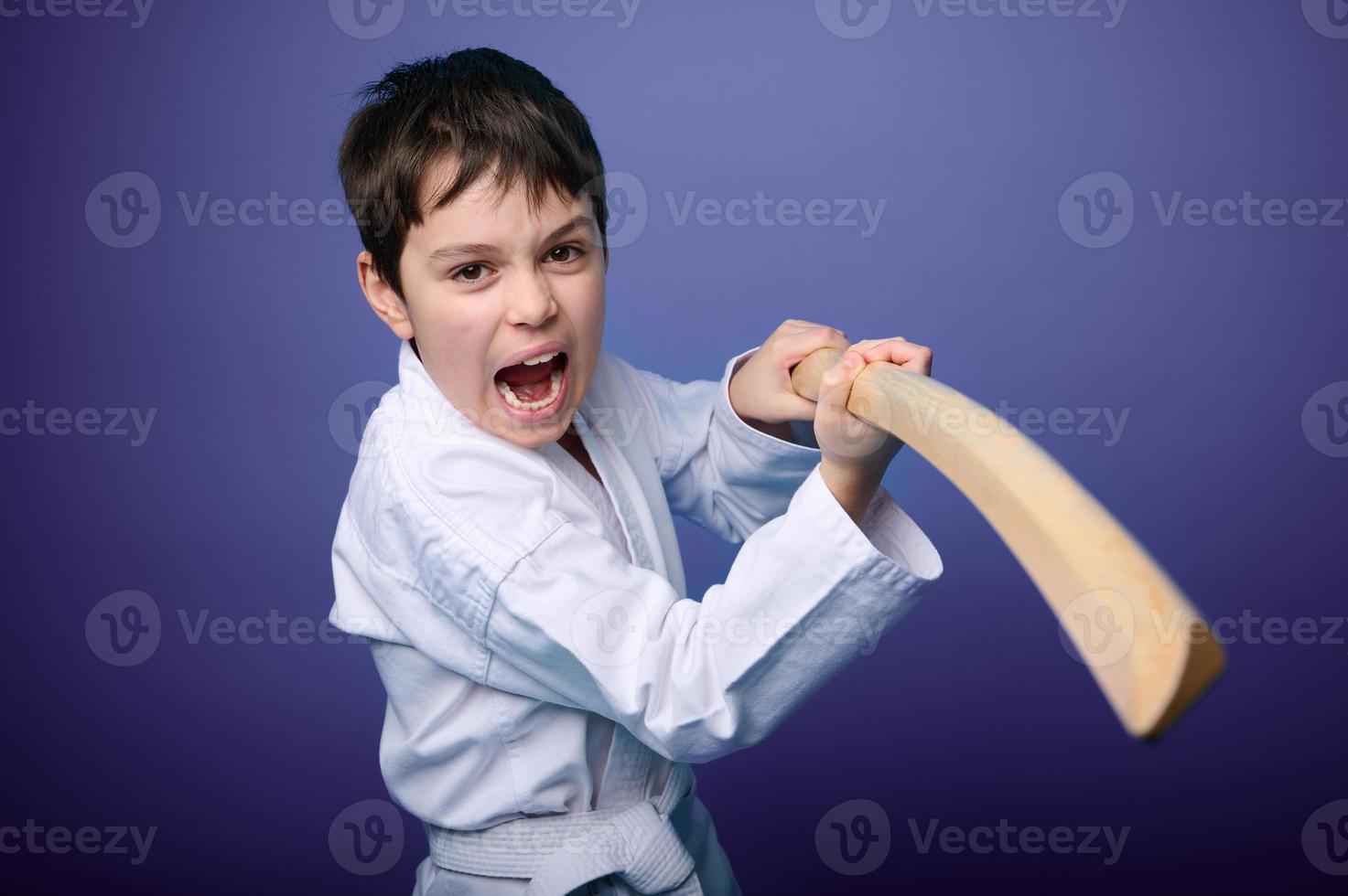 ein kaukasisch Teenager Junge im Weiß Kimono Stehen im Kampf Pose mit hölzern Katana Schwert. Aikido Kämpfer. orientalisch kriegerisch Kunst Konzept foto