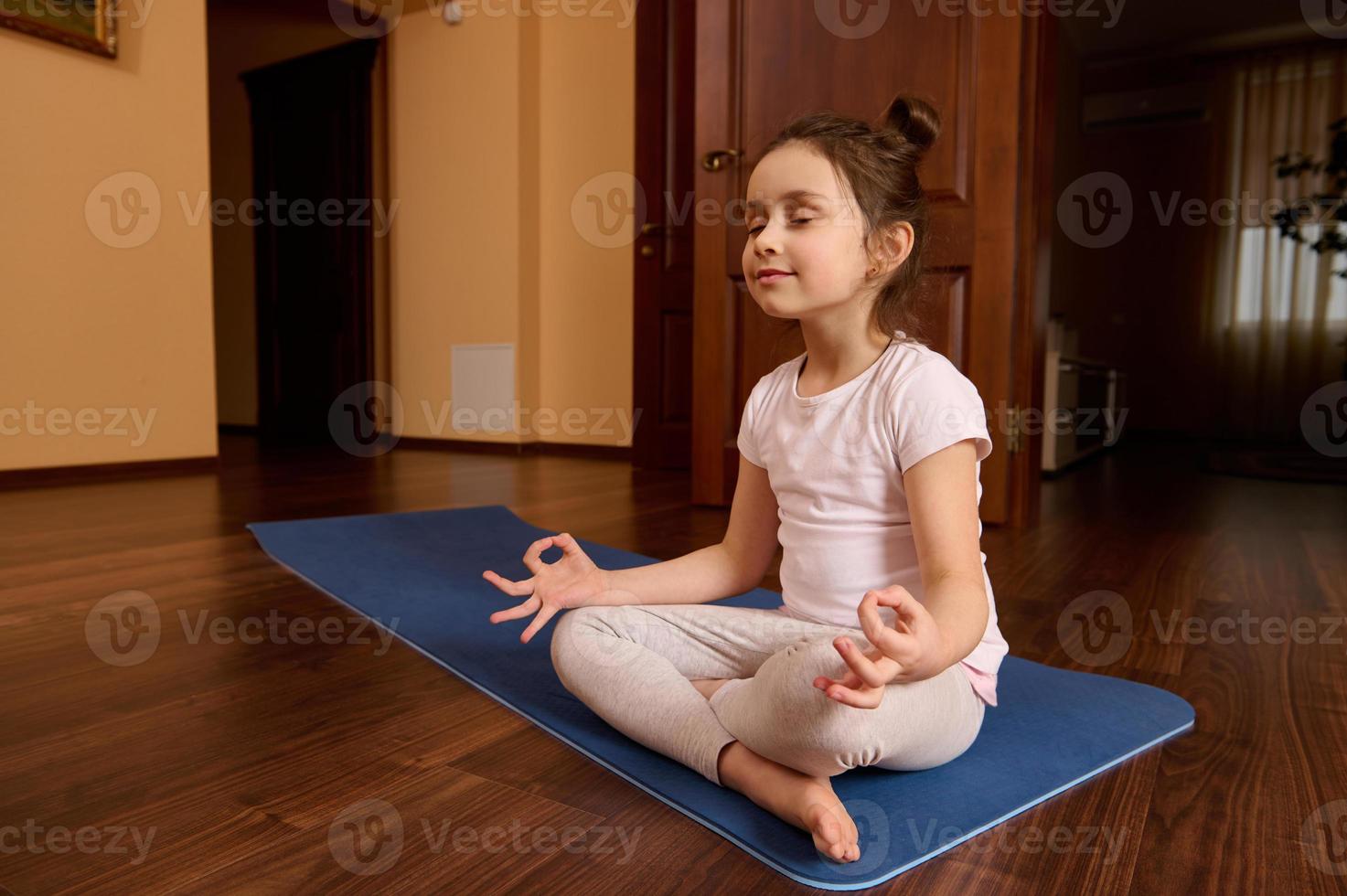 bezaubernd achtsam friedlich wenig Kind Mädchen, 5-6 Jahre alt meditieren im Lotus Pose mit Mudra Geste und geschlossen Augen foto