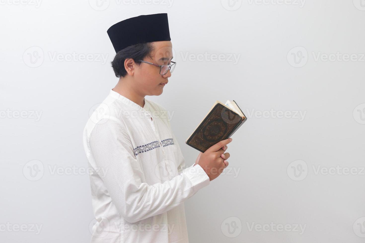 Porträt von jung asiatisch Muslim Mann lesen und rezitieren heilig Buch von Koran ernsthaft. isoliert Bild auf Weiß Hintergrund foto