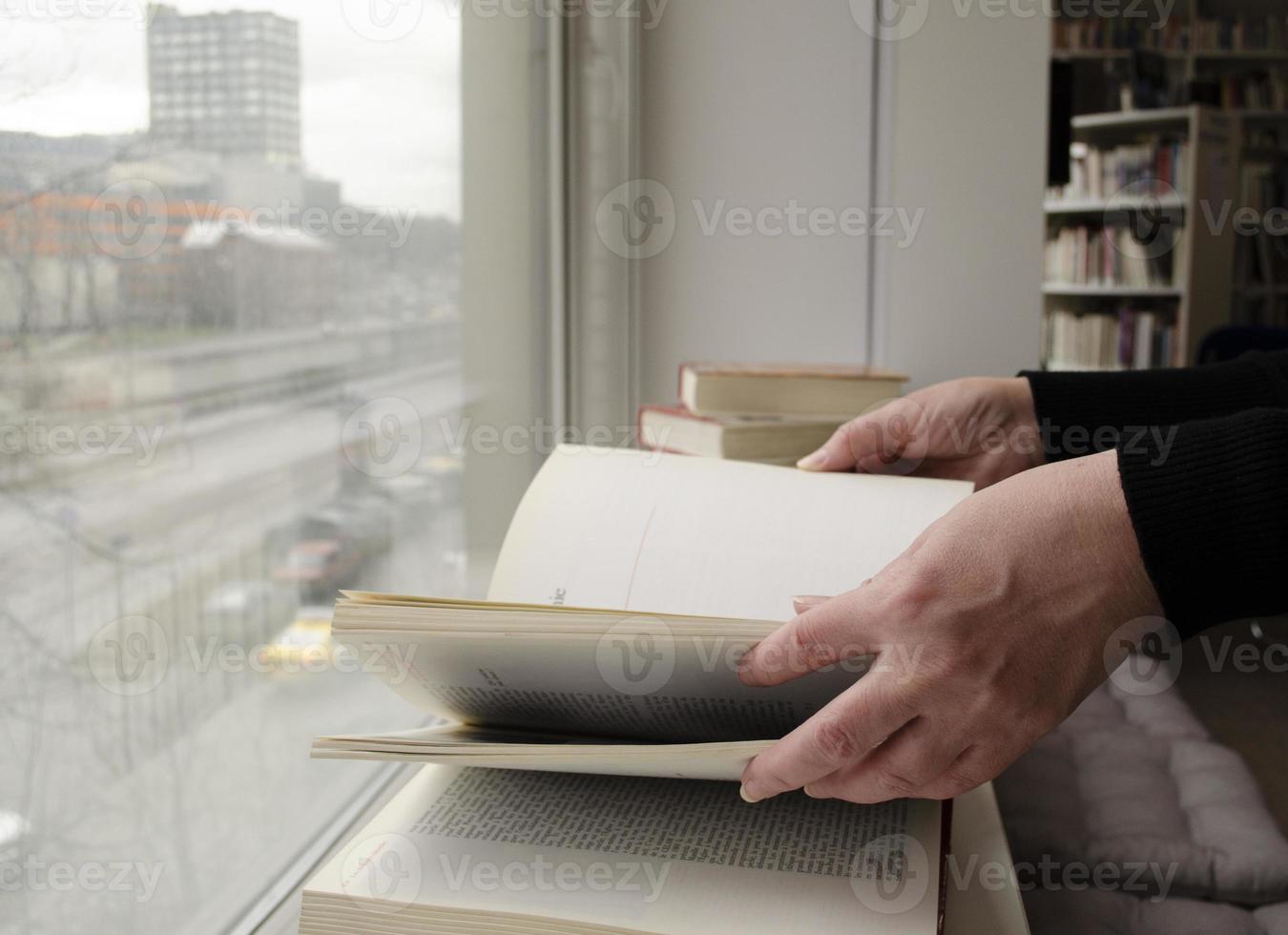 ein Person lesen Bücher in der Nähe von das Fenster. Hände wendet sich Über Buch Buchseite. foto