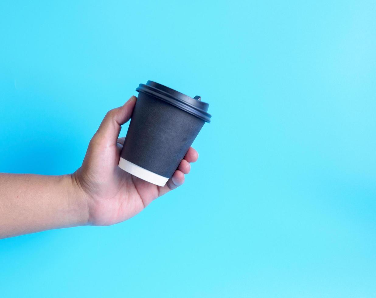 Nahansicht jung Erwachsene Mann Hand halten Weiß Tasse Papier von Kaffee heiß trinken bereit zu trinken erfrischend. Aroma Erwachen frisch zu Arbeit platziert auf ein Blau isoliert Hintergrund. Punkt von Aussicht Schuss. foto