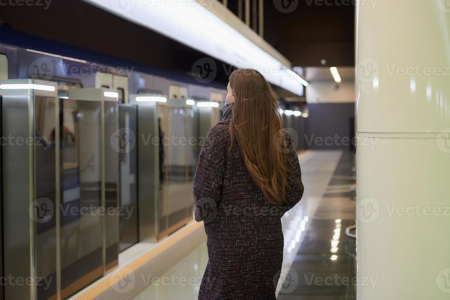 Ein Mädchen in einer chirurgischen Gesichtsmaske hält soziale Distanz zu einer U-Bahnstation foto