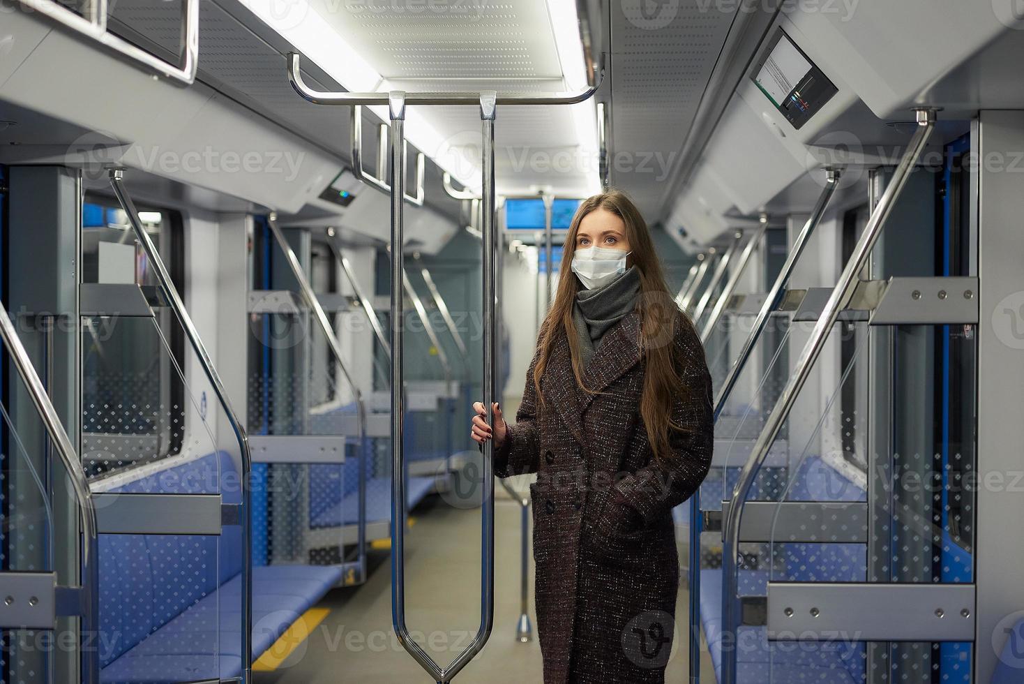 Eine Frau in einer medizinischen Gesichtsmaske hält in einem modernen U-Bahnwagen soziale Distanz foto