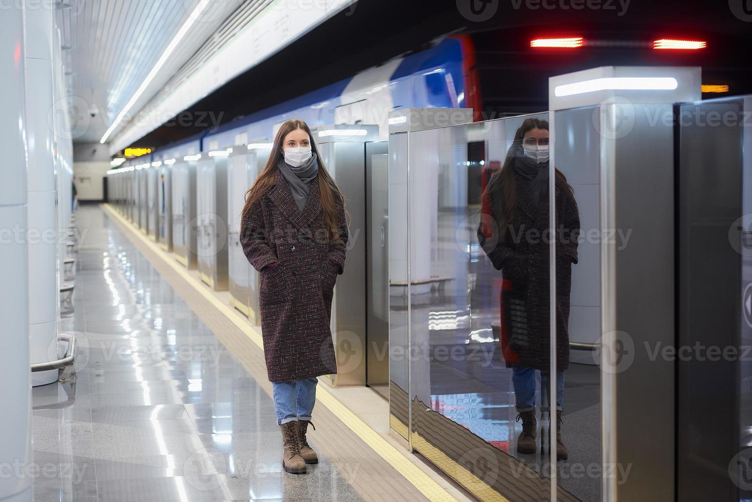 Frau in einer medizinischen Gesichtsmaske steht in der Nähe des abfahrenden Zuges in der U-Bahn foto